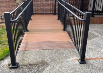 A wooden ramp with black metal railings leads to the entrance of a brick house.